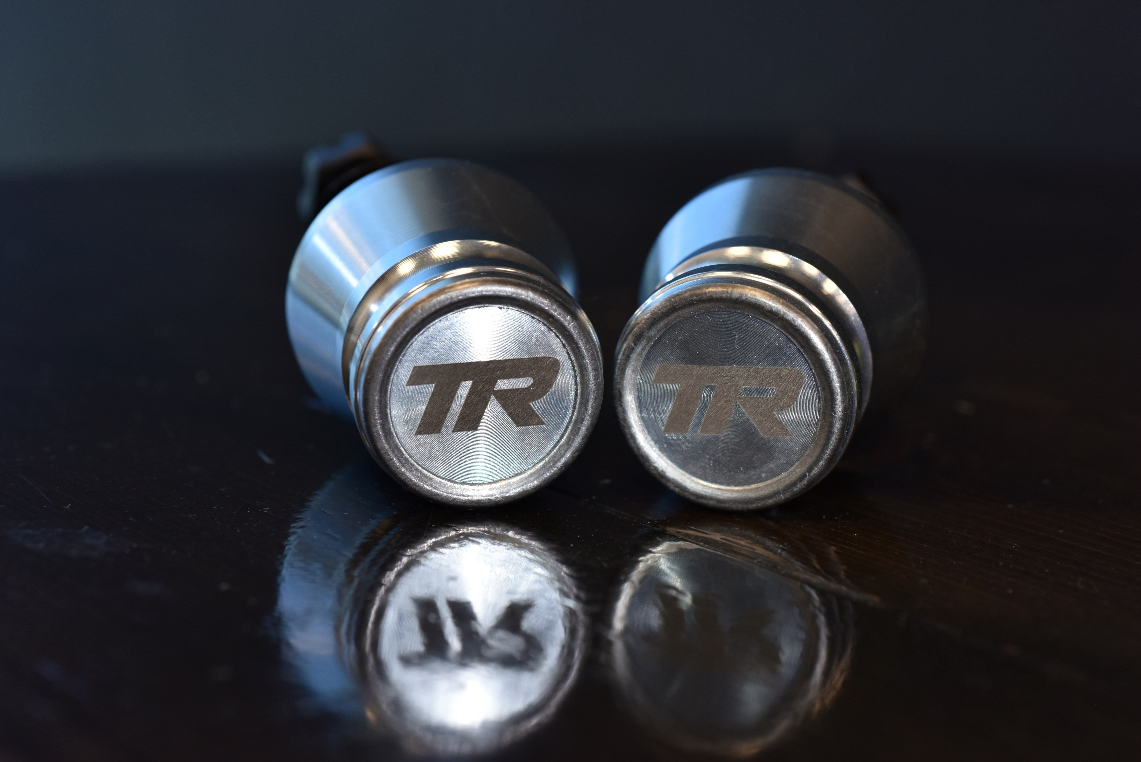 Two metallic valve stem caps with 'TR' logo on a reflective surface.